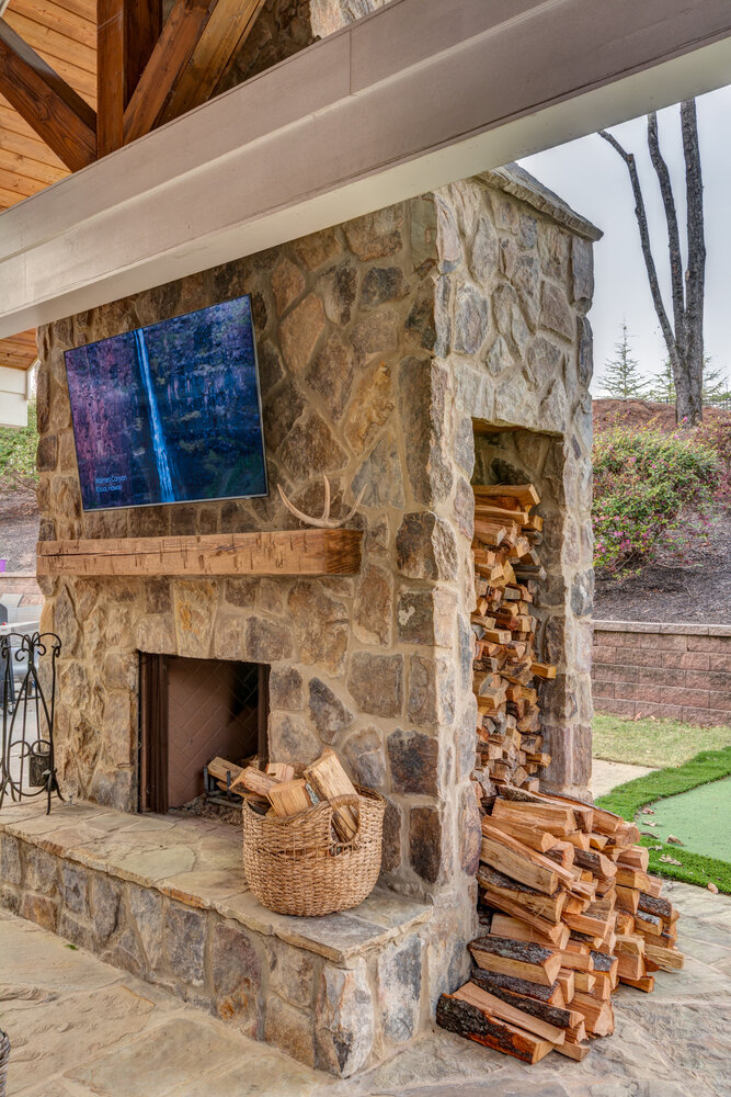 Covered outdoor stone fireplace with TV and firewood storage, remodeled by Silver Oak in Roswell, GA