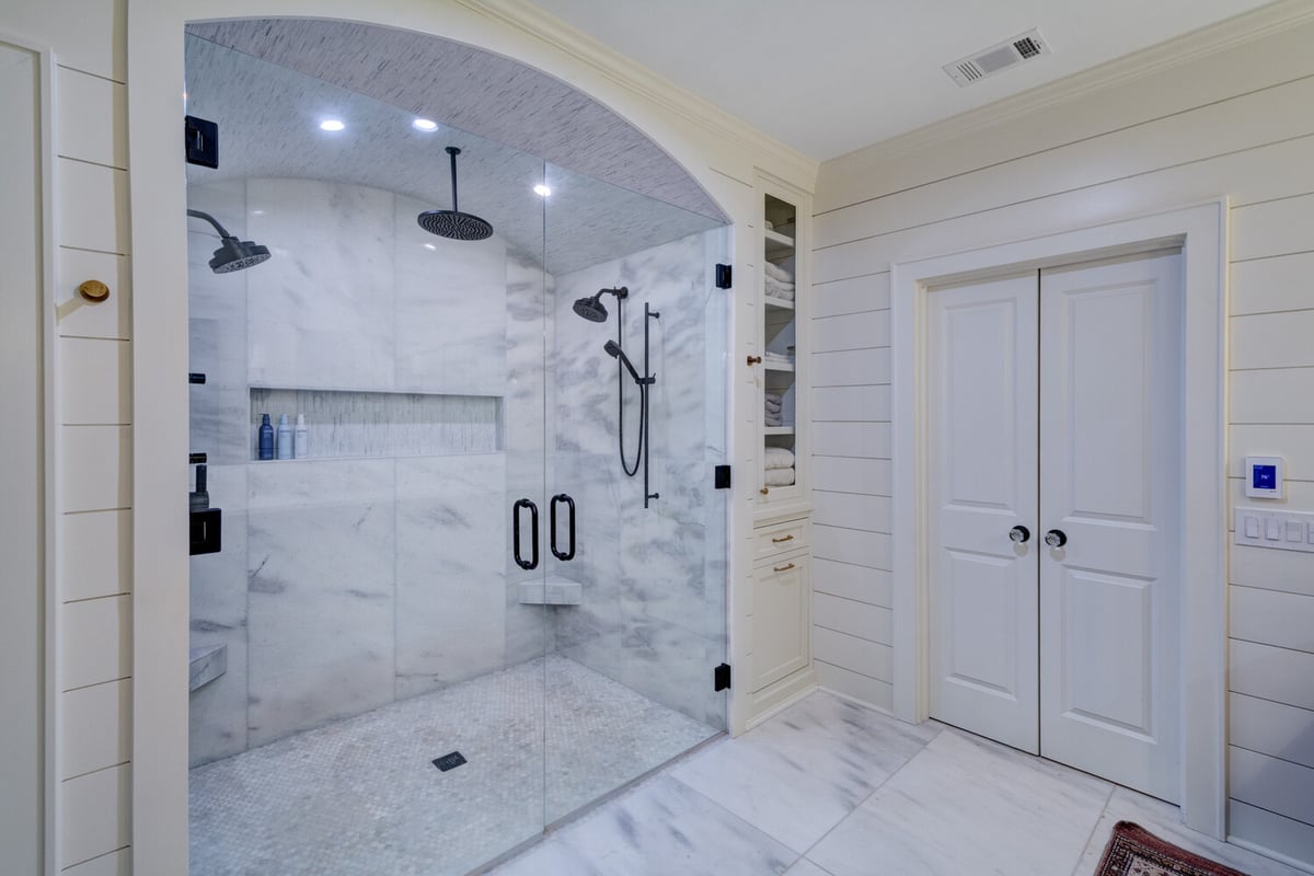 Spacious marble shower with dual rain heads and glass doors remodeled by Silver Oak in Roswell, GA