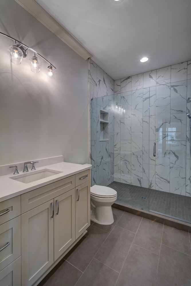 Modern basement bathroom with walk-in shower and marble-style tile by Silver Oak Remodel in Greater Atlanta