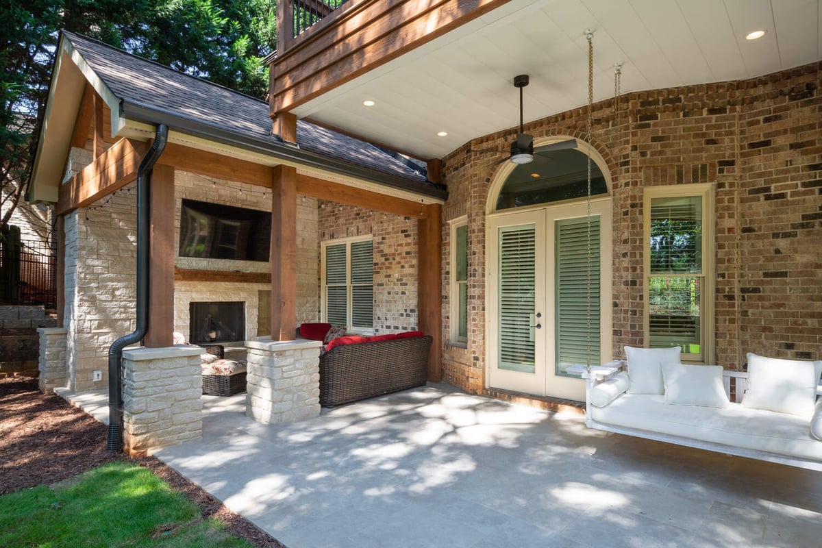Cozy covered patio with white swing and stone fireplace by Silver Oak Remodel in Atlanta, GA
