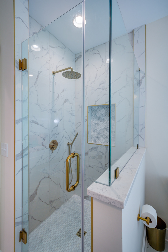 Frameless glass shower with gold accents and marble tile walls by Silver Oak Remodel in Greater Atlanta