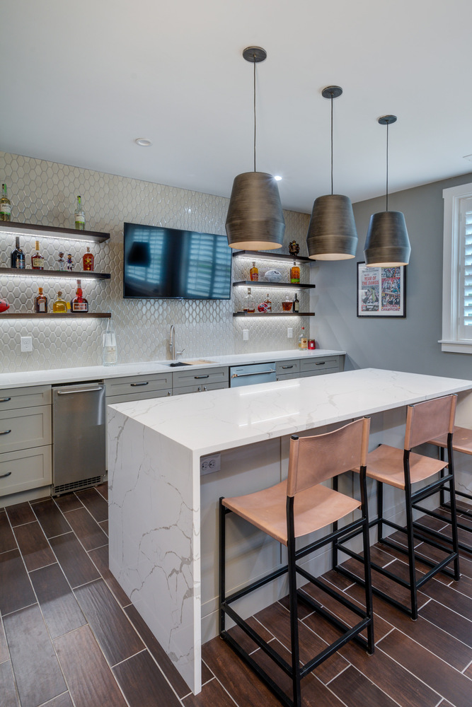 Marble waterfall bar and industrial-style lighting in a custom basement remodel by Silver Oak Remodel in Greater Atlanta